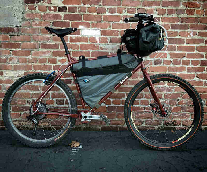 Right profile of a Surly bike, with gear, on pavement in front of a red brick wall