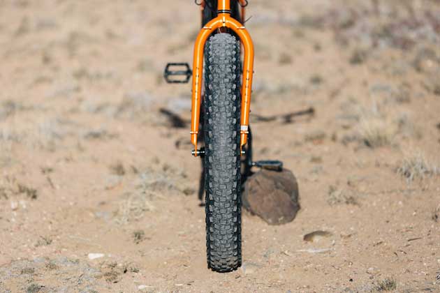 Front, head tube down view of an orange Surly Pugsley fat bike, parked on desert sand