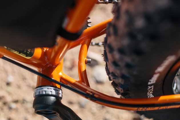 Zoomed in downward partial view of the left crank arm, seat tube, chain stay on a Surly Pugsley fat bike, orange