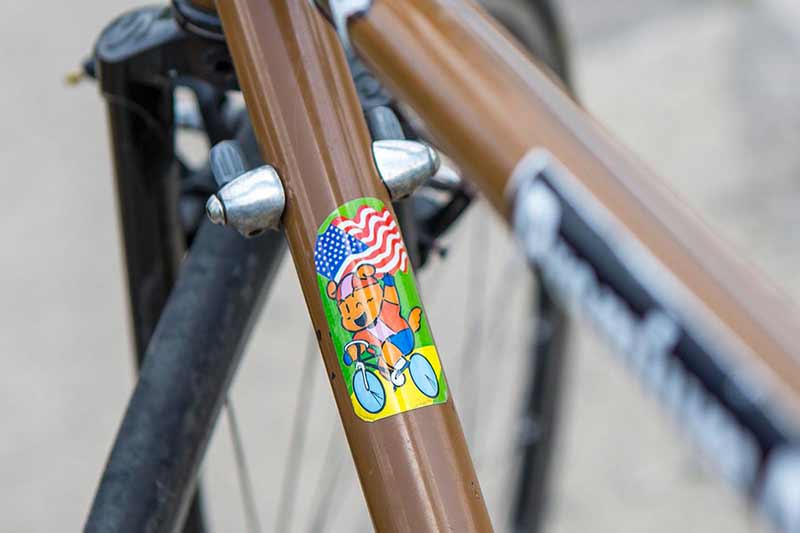 Close-up of brown Surly bike with sticker on downtube of cartoon animal biking one-handed and holding American flag