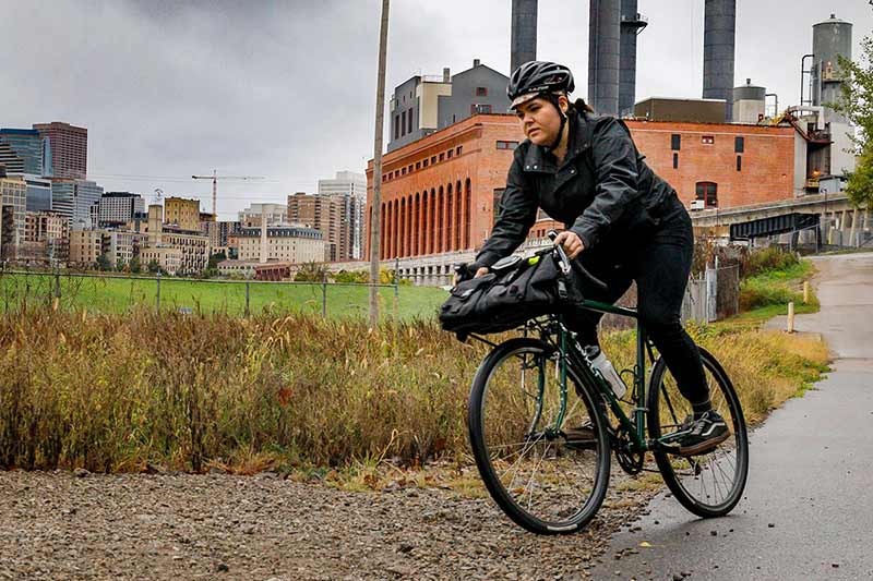 Urban commuter cyclist wearing helmet riding with bag on front rack turning off paved trail