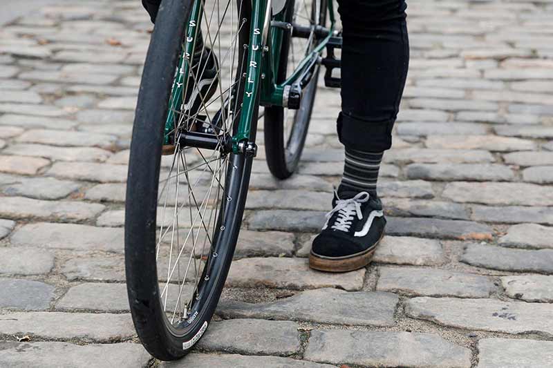 Cyclist standing over bike with one foot down on brick road