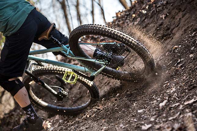 Mountain biker with knee pads riding corner with one foot off pedal, rear tire sliding and kicking up dirt