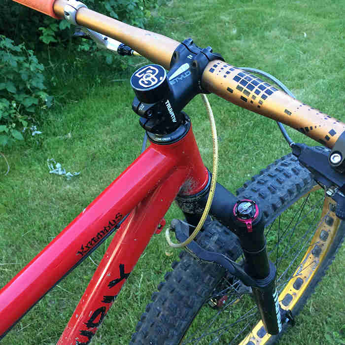 Right side downward cropped view of the front end of a Surly Krampus bike, red, with green grass below