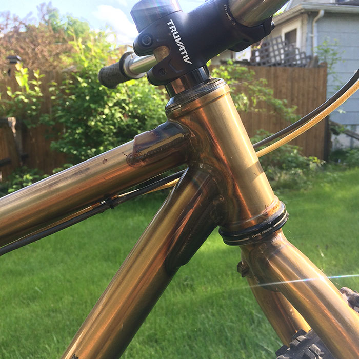 Right side close up cropped view of the head tube, top tube and down tube of a Surly Krampus OPS bike, gold