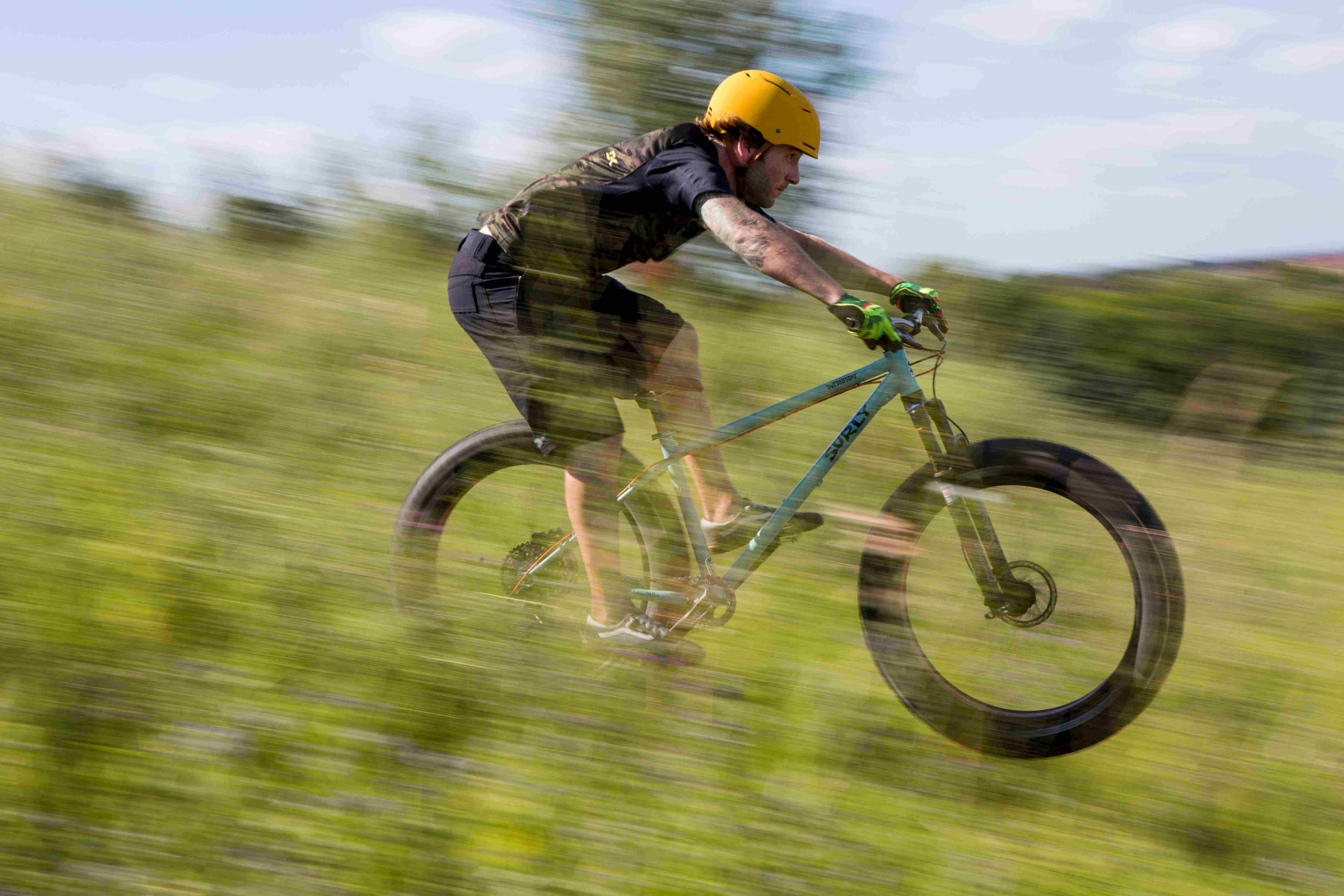 Right side blurred view of a cyclist, on a light blue Surly Wednesday fat bike, riding down a grassy hill