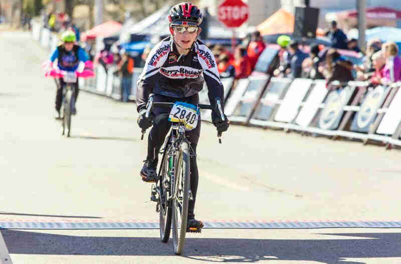 Front view of a cyclist riding a green Surly Cross Check bike across a finish line of a road race