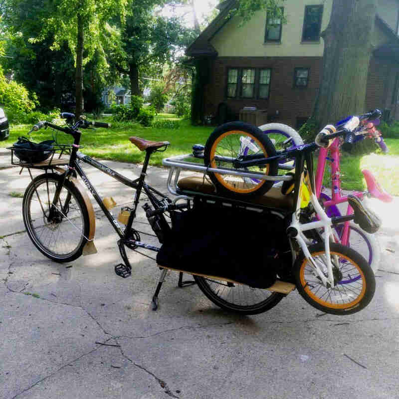 A Surly Big Dummy bike with 2 bikes hanging from the rear rack, parked in the middle of a street - left side view