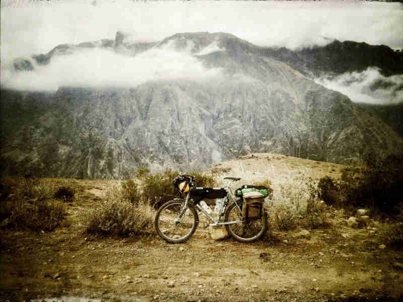 Left side view of a Surly bike, loaded with gear, parked on a gravel roadside in the mountains