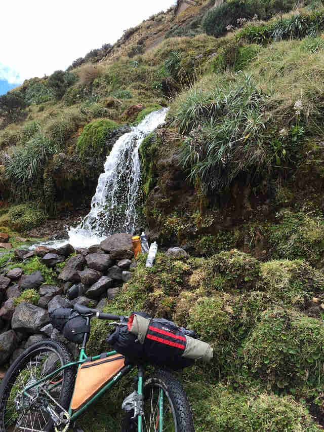 Right side view of a Surly Krampus bike, against a grassy hill, with a small waterfall above in the background