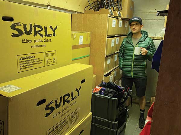 Matt in storage room stacked with bike boxes and bike parts