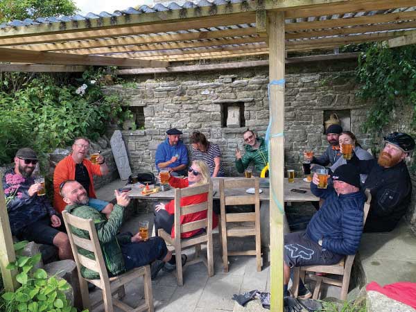 Cyclists sitting at outdoor pub table having a pint and posing for photo