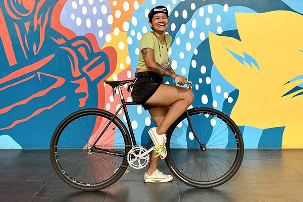 Aneka on Surly Steamroller bike with one foot down, smiling, in front of mural