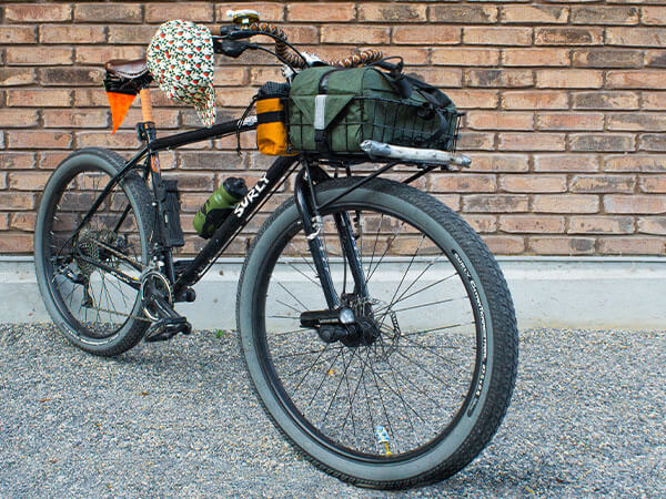 Front three-quarter view of Abner's custom built Bridge Club bike with loaded front rack/bag, leaning against building