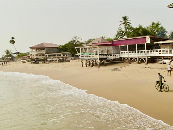 Beach front buildings, Slim Wonder standing on sand beach with bike and waves come in