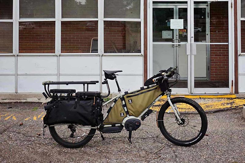 Right side view of a white Surly Big Easy bike loaded with gear on a parking lot in front of a building with glass doors