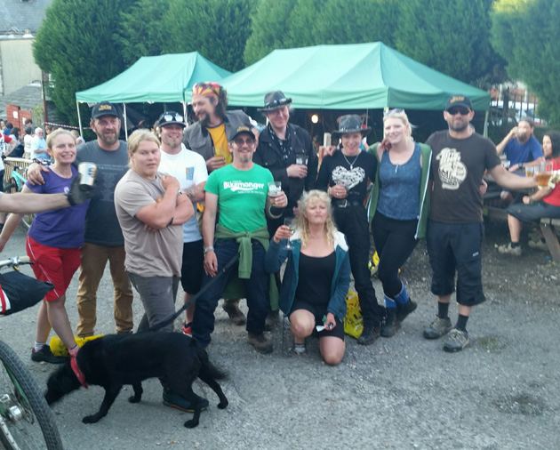 A group of people and a black dog looking ahead with people and a green canopies in the background