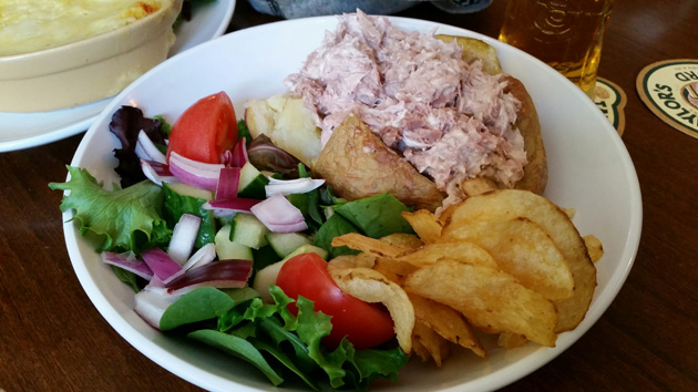 White bowl of potato chips, a mixed salad and a sandwich rolls sitting on a table