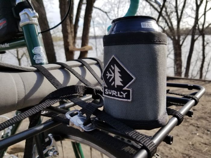 Zoom in of a can in a Surly can cooler mounted to the front rack of a bike with trees and lake in the background