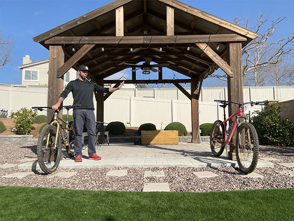 Colin in backyard gazebo holding rigid Karate Monkey with open hand out to Salsa Timberjack with suspension fork