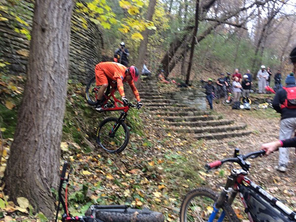 Cyclist descending steep rock wall to dirt transition while people watch