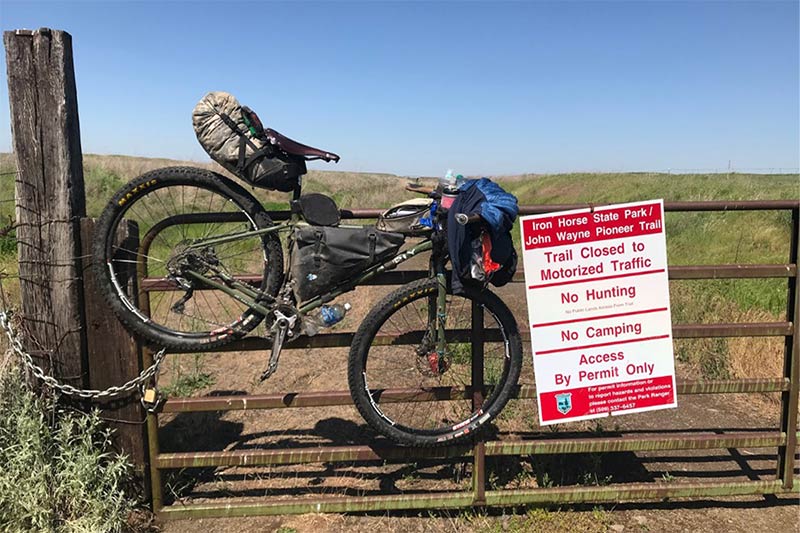 Fully loaded Surly with bikepacking bags propped up hanging from cattle gate on gravel road