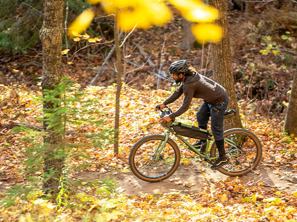 Person riding Grappler with small frame pack on forest singletrack, leaves on the ground