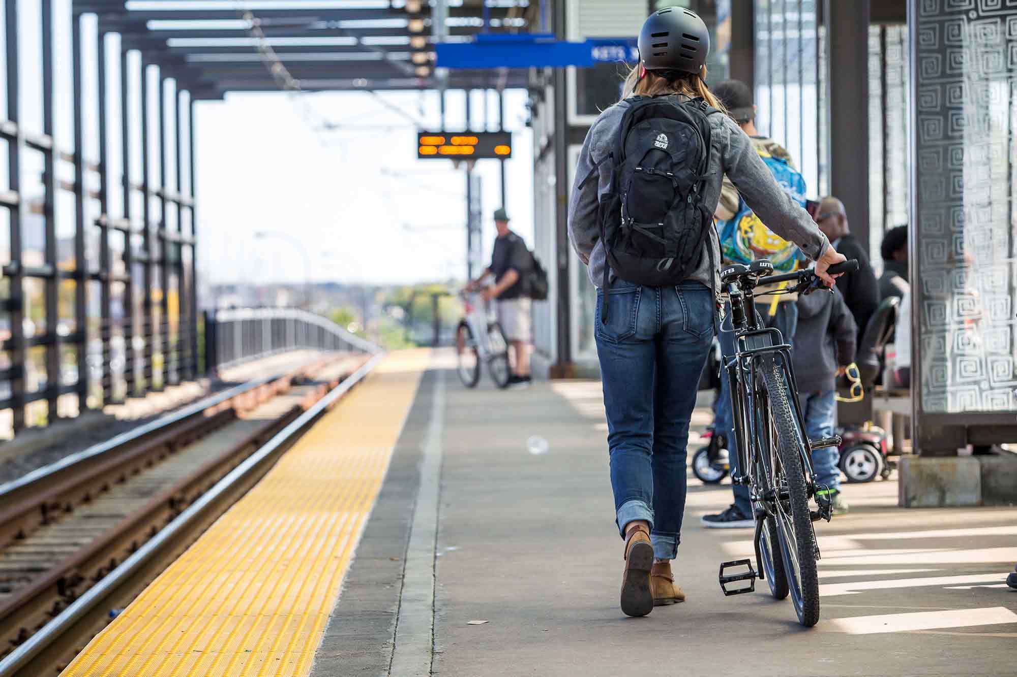 Cyclist with backpack and helmet walking bike to commuter train stop