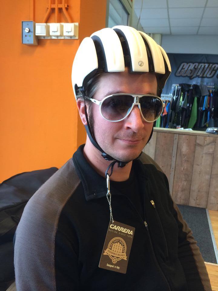 Head shot of a person wearing a bike helmet and sunglasses, with an orange wall and a counter in the background