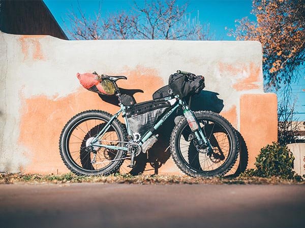 Blue Surly Wednesday loaded with framepack and bags for bikepacking, parked against wall in sun