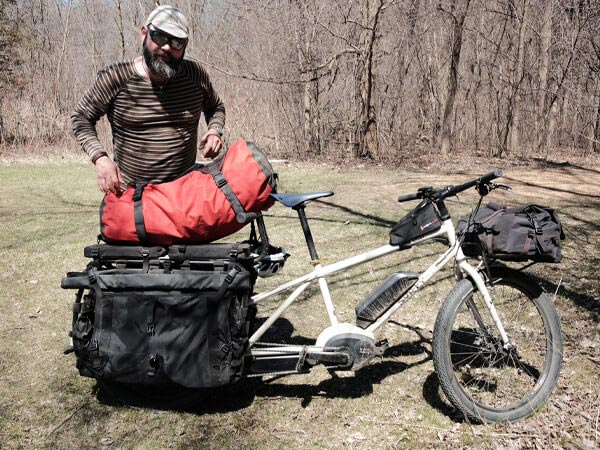 Person loading parked Surly Big Easy with large dry bag at camp site on sunny day