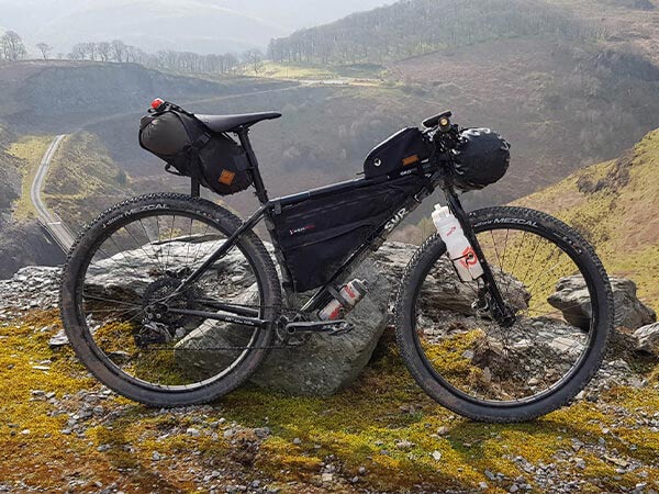 Black Surly Karate Monkey parked against rock atop mountain overlook loaded with various bags and framepack for bikepacking