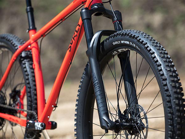 Orange Surly Krampus with RockShox suspension fork and dropper seatpost out in sun, front three-quarter view