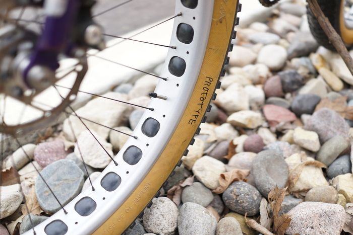 Downward angle view of 25 percent of a brake disc on a fat bike rim and tire with the word prototype sitting on rocks