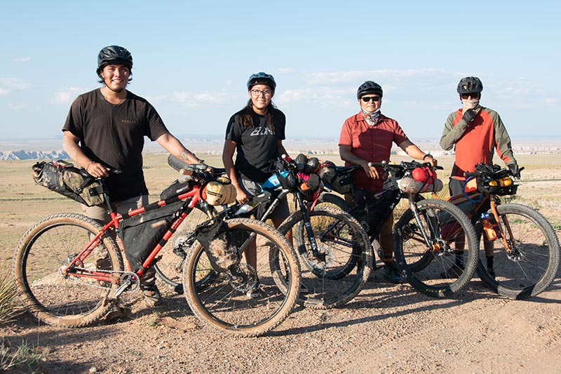 Four mountain bikers standing with their loaded bikes for a group shot on mesa