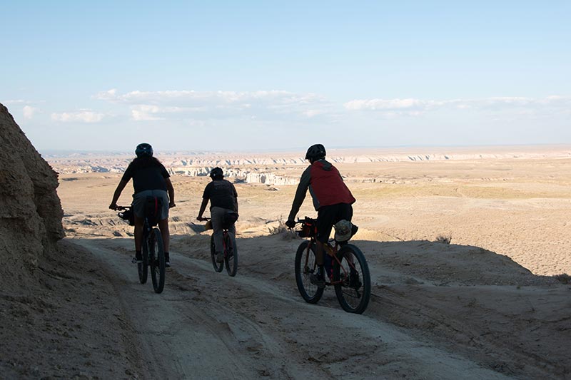 Three mountain bikers descend rutted gravel road toward the open mesa