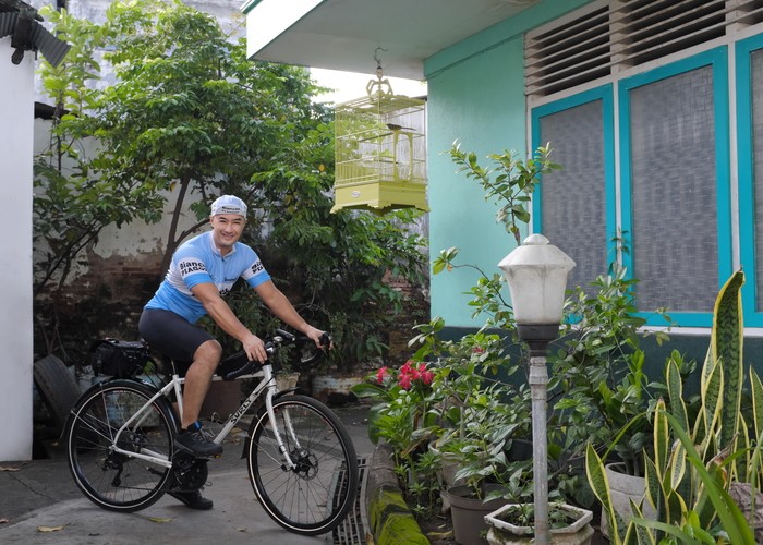 Cyclist sitting a white Surly Midnight Special bike with a seat pack poses in front of a home with plants and shrubbery