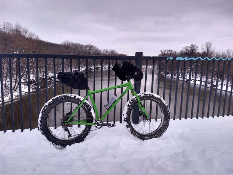 Surly Ice Cream Truck bike, green, with seat pack and water bottle, in snowy field with buildings in background