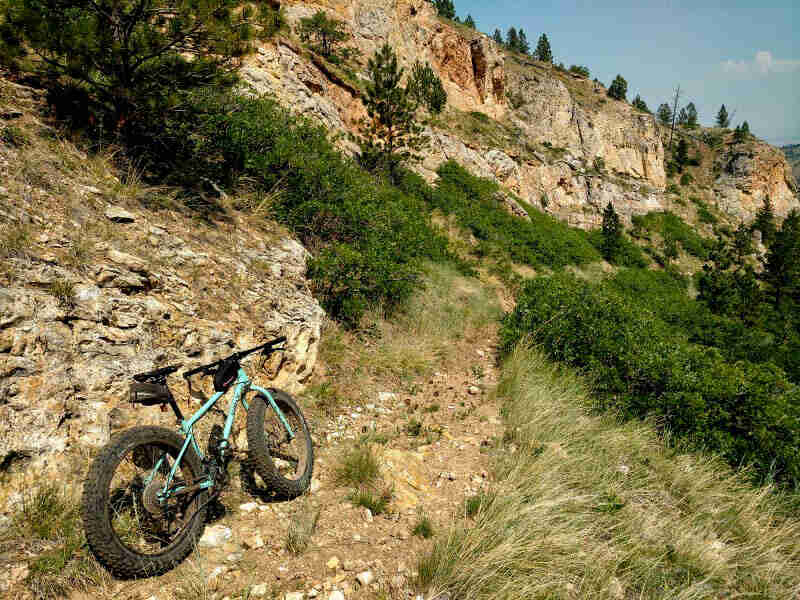 Rear right side view of a Surly Wednesday MY17 fat bike, mint, parked on a rocky trail, facing up a mountain