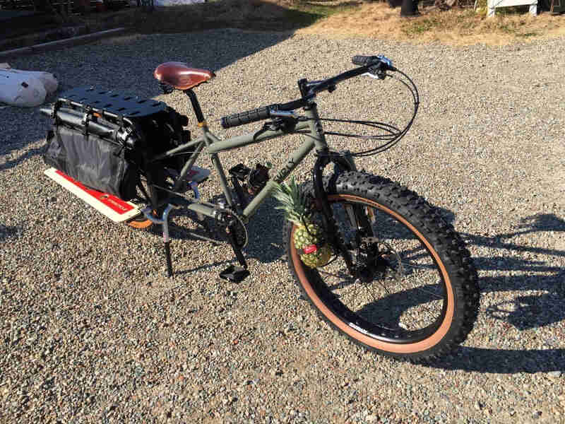 Downward right side view of a Surly Big Fat Dummy bike, olive, parked in a gravel lot