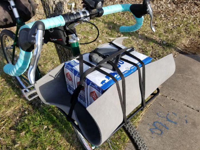 Downward view of a green Surly Pack Rat bike with front rack carrying a 12 pack of beer and Surly can cooler