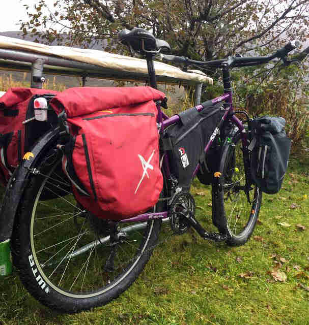 Rear right view of a purple Surly Troll bike, in the grass, leaning on a fence post, with trees in the background