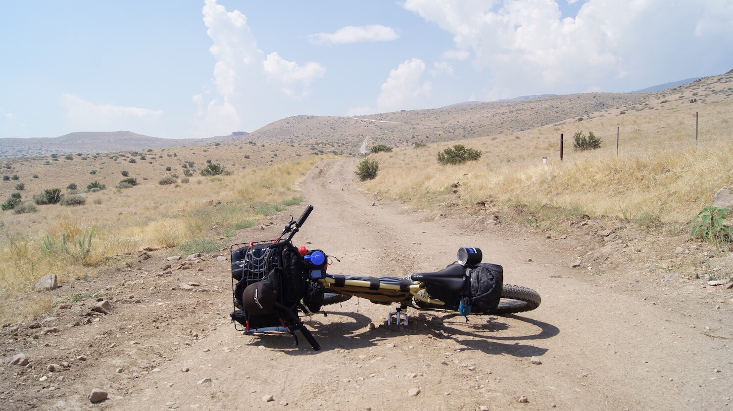 A bike laying across a gravel road with brown, grassy hills in the background