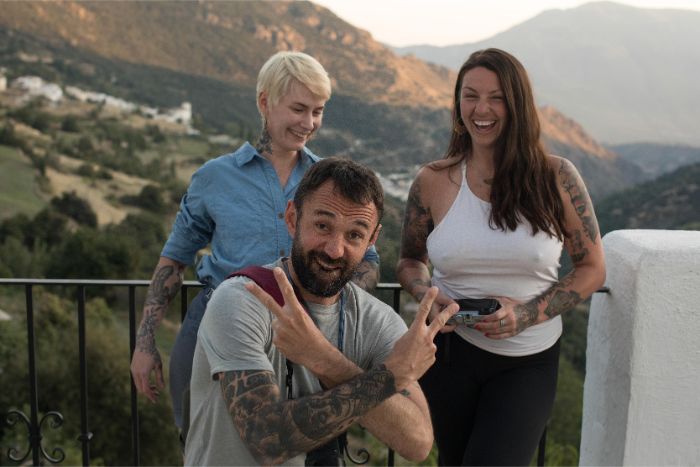 Three friends posing on a patio in the mountains with one kneeling giving peace signs with hands