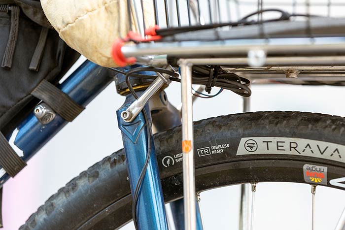 Detail showing front rack and basket mounted to fork crown, sidewall of front tire, frame bag lower straps to downtube and dynamo wire going from front hub to front light