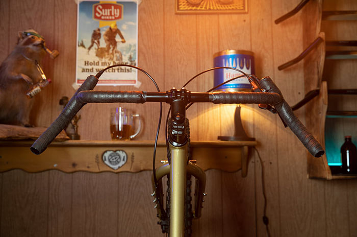 Surly Corner Bar with black bar tape up on gold Surly Karate Monkey against wood paneled wall with beer mug in background