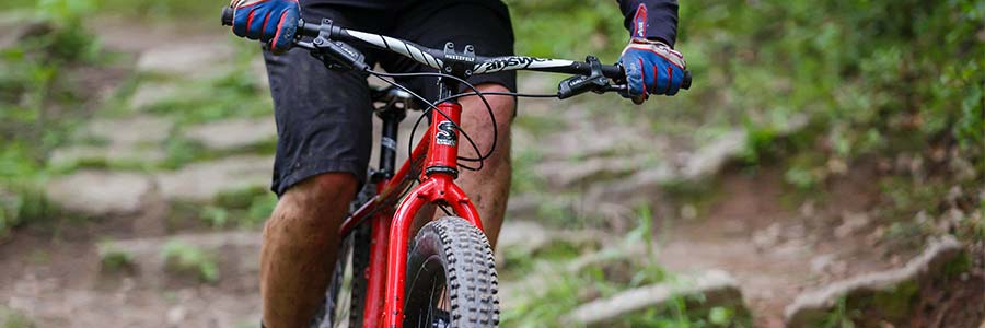 Mountain biker on rocky off-road trail riding red Surly Krampus showing large Surly Dirt Wizard tires on wide rims