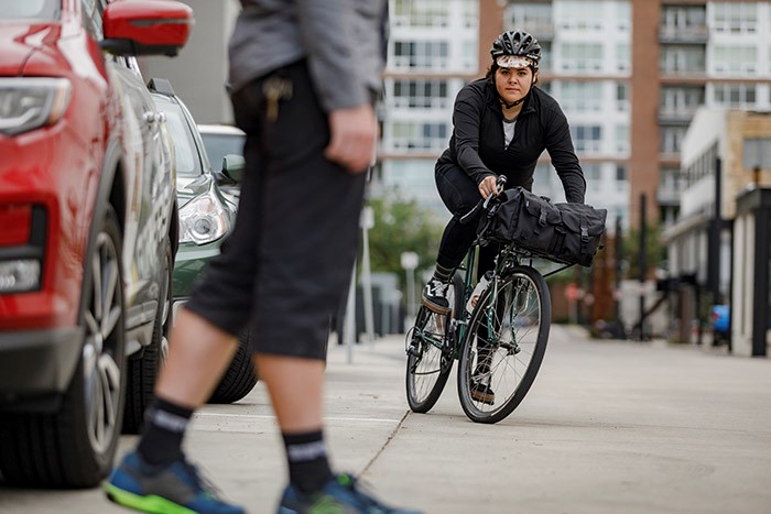 Front view of a cyclist on a green Surly Pack Rat bike, swerving around a person, with city buildings in the background