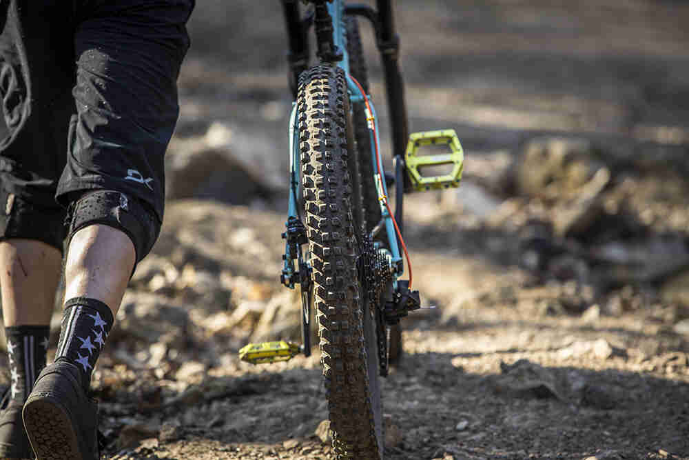 Rear cropped view of the legs of a cyclist walking on the left side of their bike down a gravel trail