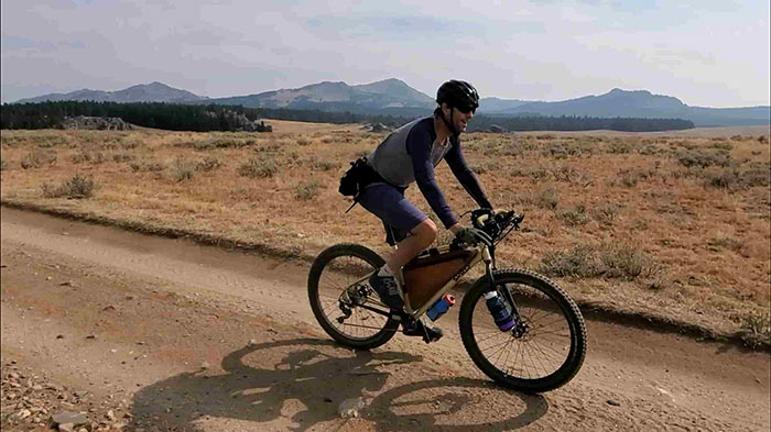 Person riding gold Surly Karate Monkey with Corner Bar on desert gravel road with mountains in background